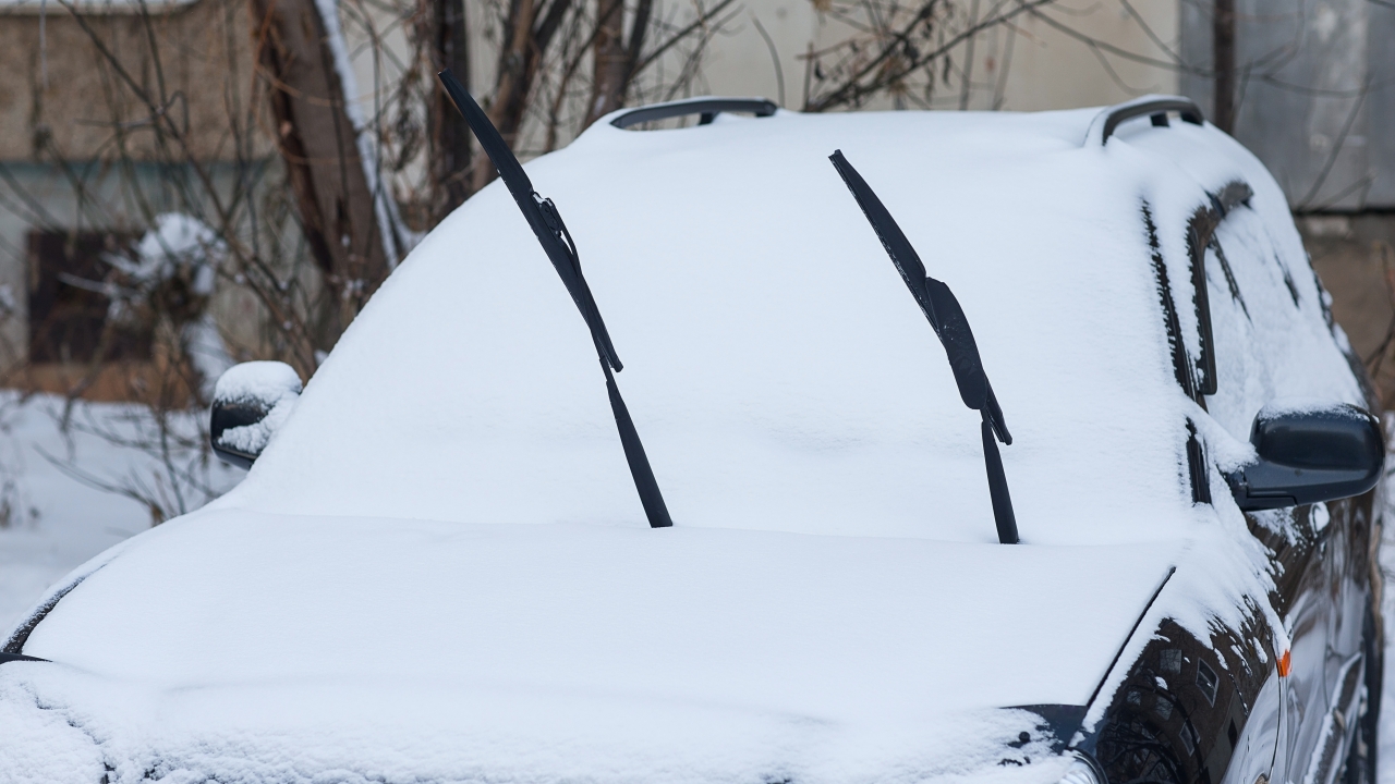 Windshield wipers stick up from a snow-covered car
