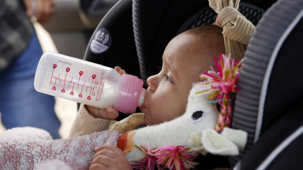 A baby drinks from a bottle after being buckled into her car seat.