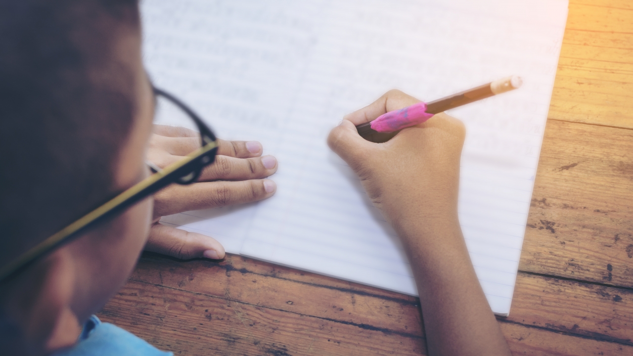 Kid's hand with pencil writing on notebook